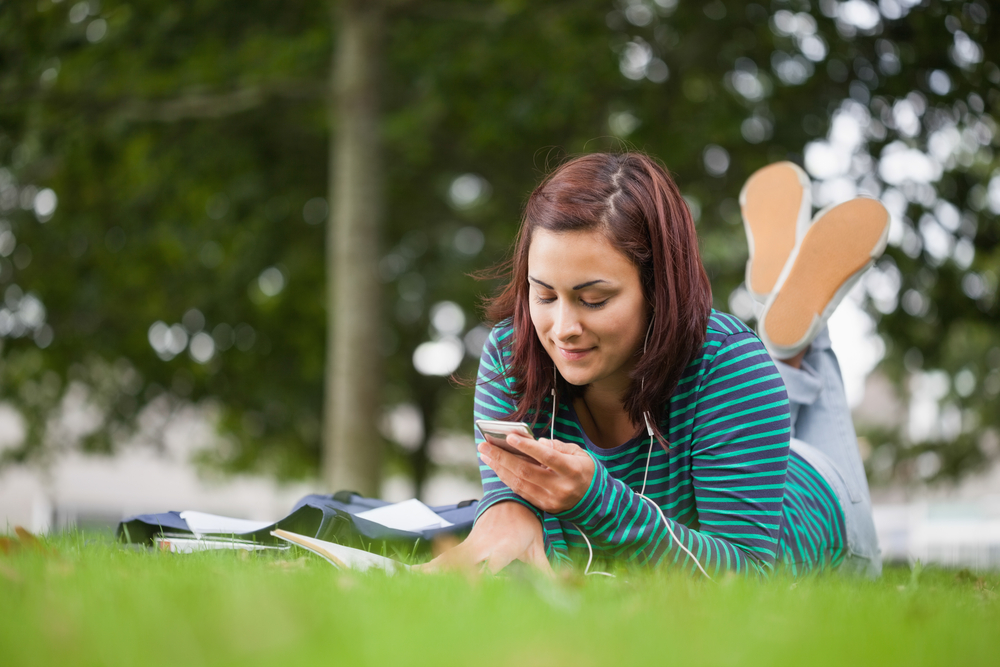 Attractive casual student lying on grass texting on campus at college Attractive casual student lying on grass texting on campus at college